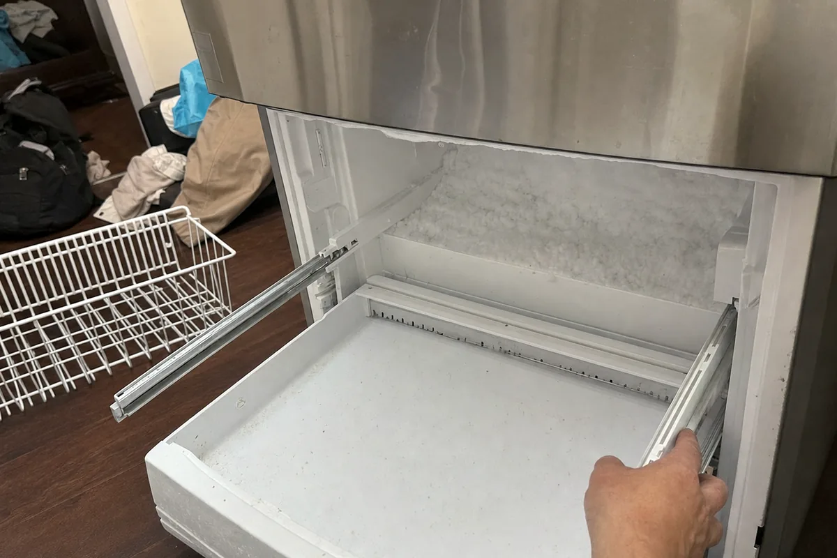The open lower drawer of a built-in freezer with its basket removed, the runners and the cabinet floor exposed