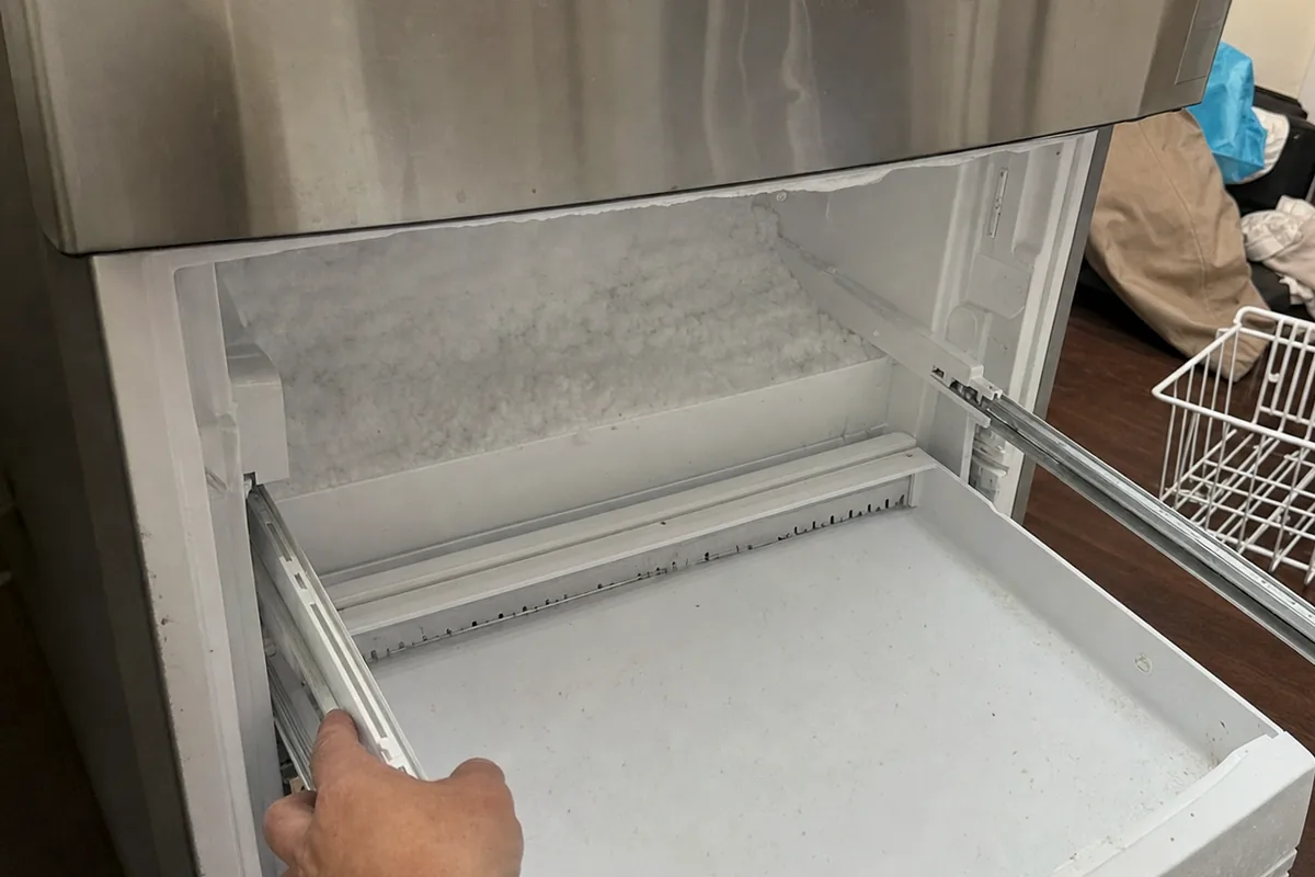 Close view of an empty freezer drawer showing an even layer of frost across its floor and sides