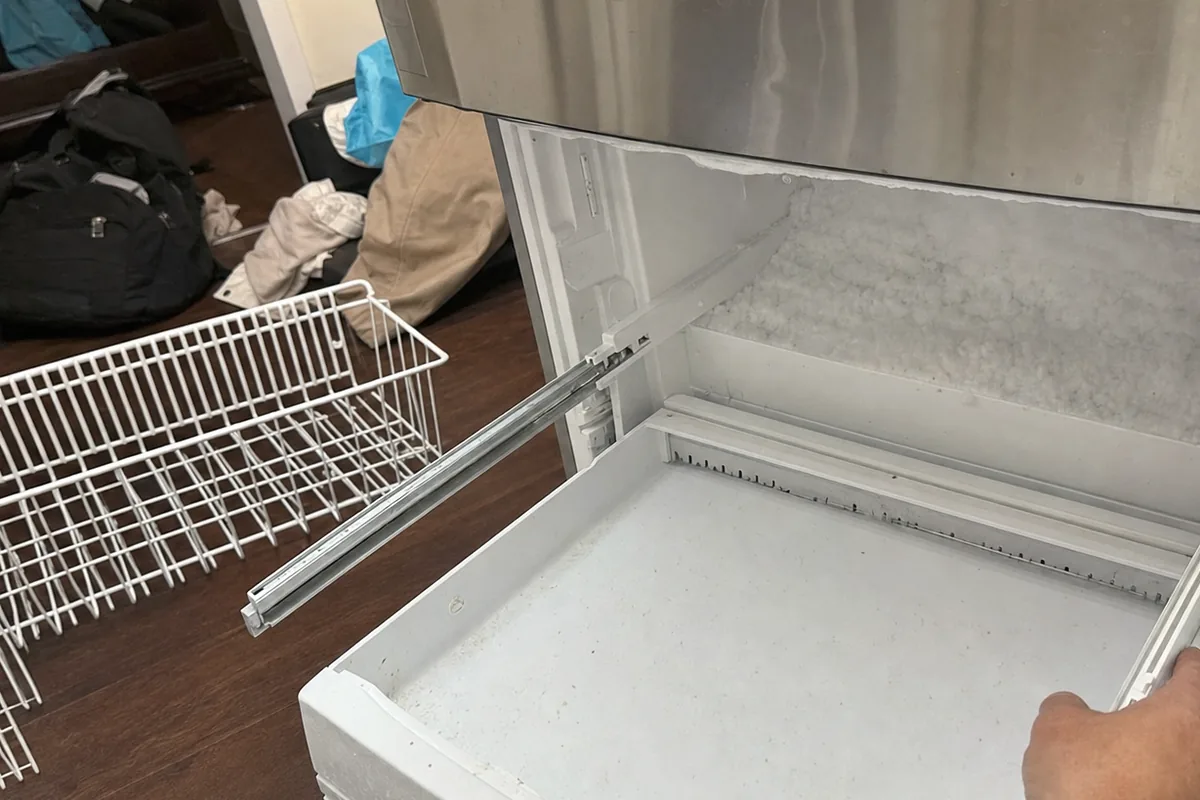 A stainless freezer drawer half withdrawn, a wire storage basket standing on the floor in front of it