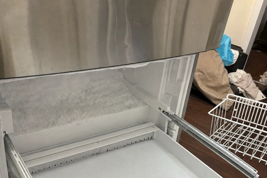 A hand steadying the edge of an open freezer drawer at the front of a built-in cabinet