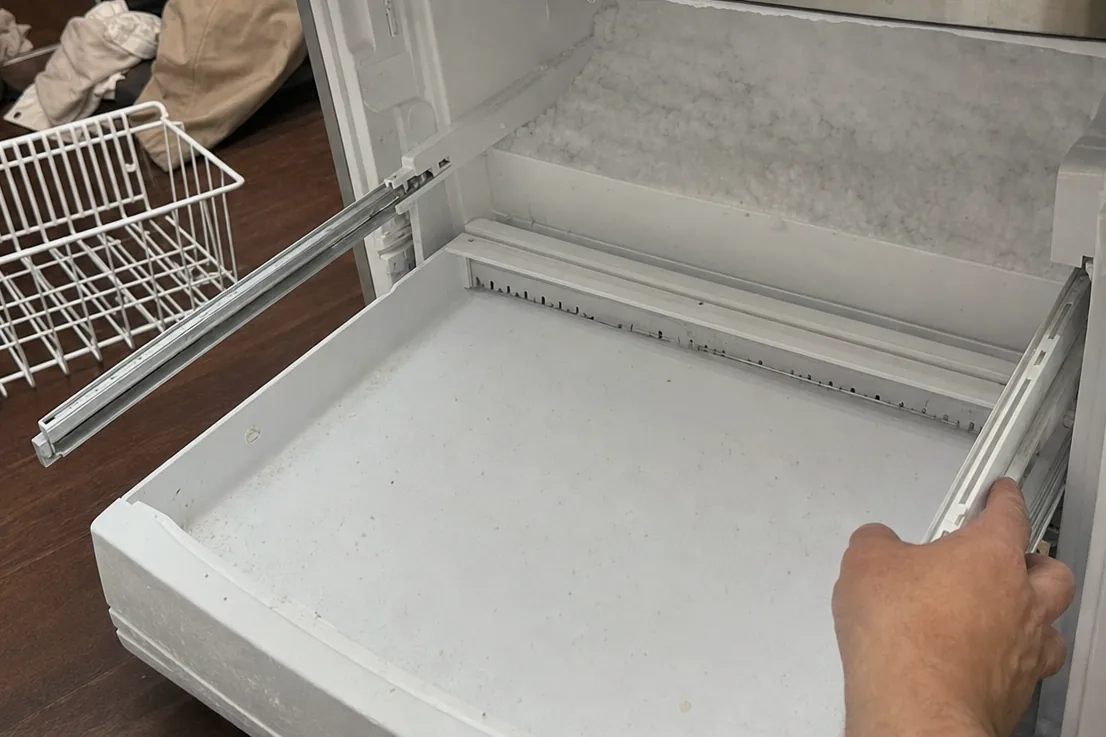 A plain, close view of an open freezer drawer and the empty basket set beside it