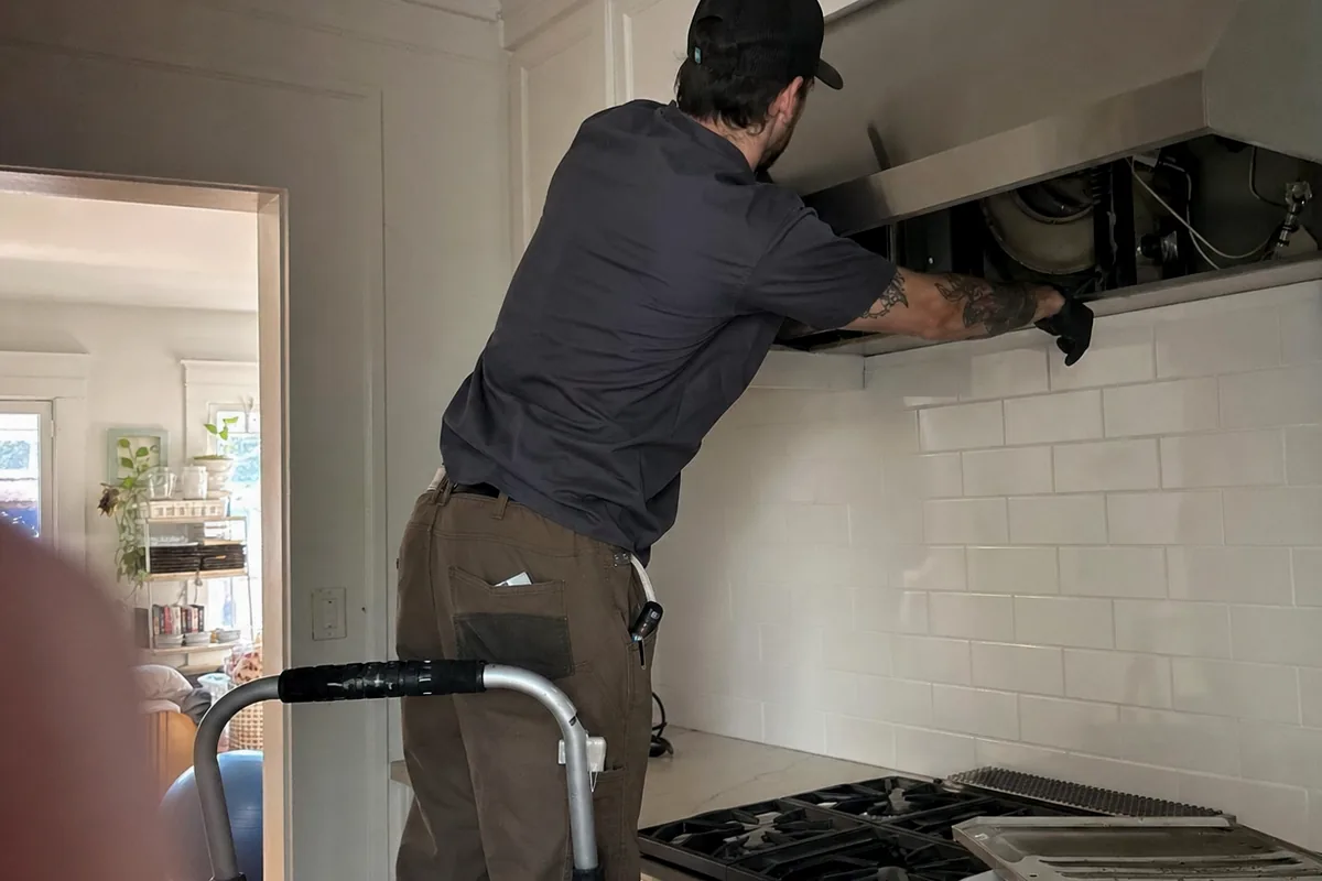 The underside of a wall-mounted hood with the technician’s hands inside the blower opening
